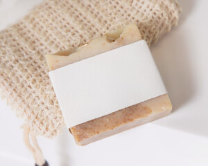 Beige handmade soap bar with blank label on soap saver bag on washbasin close up, mockup