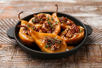 Delicious pears with caramel sauce, pecan nuts and thyme on wooden table, closeup