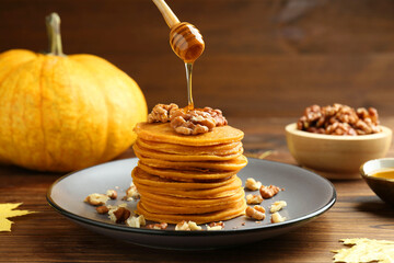 Pouring honey onto tasty pumpkin pancakes with walnuts at wooden table, closeup