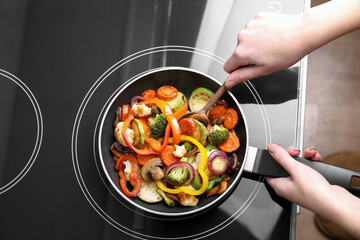 Woman cooking vegetables and mushrooms in frying pan on cooktop indoors, top view