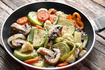 Different vegetables and mushrooms in frying pan on wooden table, closeup