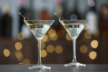 Martini cocktail with olives in glasses on wooden table against blurred background. Bokeh effect
