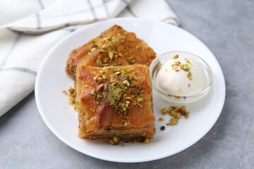 Tasty baklava with chopped nuts and scoop of ice cream on grey table, closeup