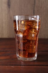 Sweet soda water with ice cubes in glass on wooden table, closeup