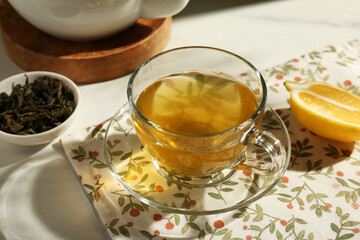 Refreshing green tea in cup, cut lemon and dry leaves on white table, closeup