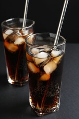 Refreshing cola with ice cubes and drinking straws in glasses on black table, closeup