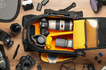Professional photographer's equipment and backpack on wooden background, flat lay