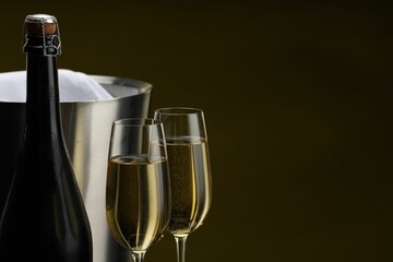 Bottle of sparkling wine, glasses and cooler bucket on brown background, closeup. Space for text
