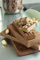 Stack of tasty Dubai chocolate bars with pistachios and knafeh on grey table, closeup