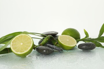 Spa composition with limes, massage stones and bamboo stem on wet surface against white background