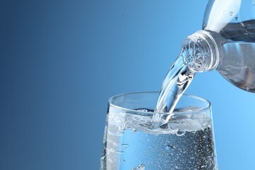 Pouring refreshing soda water from bottle into glass on light blue background, closeup. Space for text