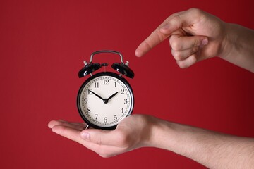 Man pointing at alarm clock on red background, closeup