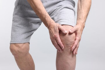 Senior man suffering from knee pain on light grey background, closeup