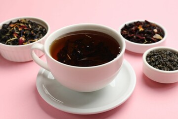 Aromatic tea and dried leaves on light pink background, closeup