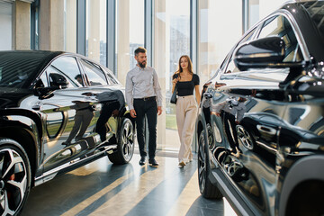 A couple of a man and a woman walk around a car dealership and choose a car
