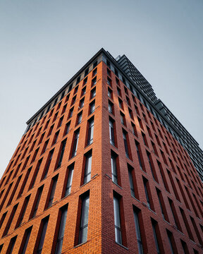 Looking up at the facade of modern building with brick facade. Corner of stylish residential building at sunset against clear blue sky. Kyiv, Ukraine - March 25 2021.