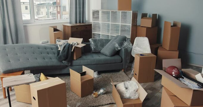 A cluttered living room filled with moving boxes and various pieces of furniture everywhere