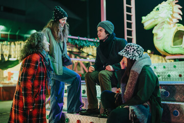 Obraz premium A group of friends gathered at an outdoor event, sharing joyous moments near a brightly lit dragon-themed ride, emanating warmth and festive spirit in the chilly evening.