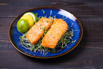 Grilled salmon fillet with microgreens on blue plate on wooden table