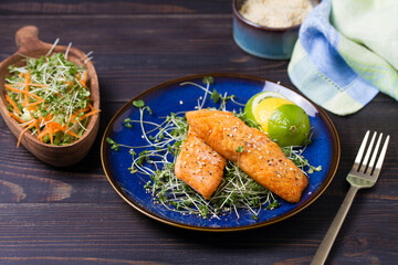 Grilled salmon fillet with microgreens on blue plate on wooden table