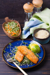 Grilled salmon fillet with microgreens on blue plate on wooden table