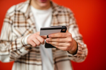 young man use credit card and mobile phone in front red background
