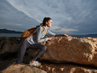 Active young woman exploring rocky coast, wearing athletic clothing and backpack, showcasing...