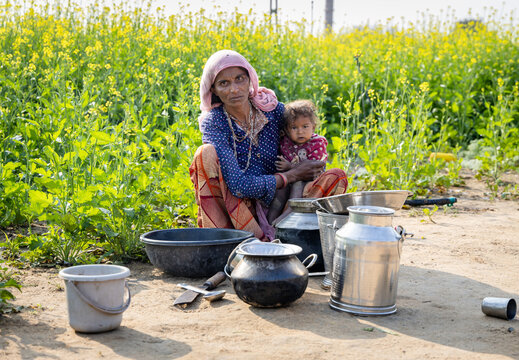 poor malnutrition village women living below poverty line holding baby with mustard fields behind