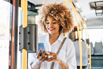 Beautiful black woman using ticket machine and paying contactless for bus or tram. Modern city lifestyle and public transportation concept. © Dusko