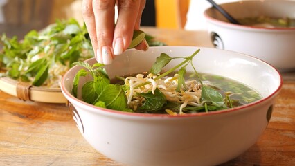 Fresh lime juice drizzled into steaming pho enhances flavor adding citrusy zest Pho preparation captures authentic Vietnamese tradition Vibrant pho bowl with rich broth fresh herbs and perfect balance