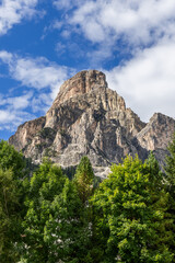 Vertical view of the rugged Sassongher mountain surrounded by dense greenery, with sunlight highlighting its rocky cliffs and alpine beauty