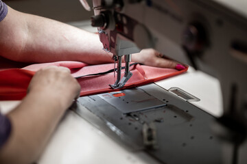 A skilled worker operates an industrial sewing machine, stitching red fabric with precision. The image highlights craftsmanship, expertise, and quality in textile manufacturing and upholstery work
