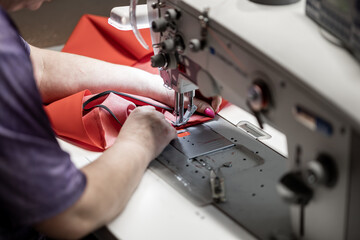 A skilled worker operates an industrial sewing machine, stitching red fabric with precision. The...