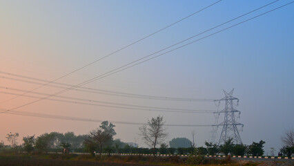 Tall metal power lines stretch across a rural landscape during dawn.