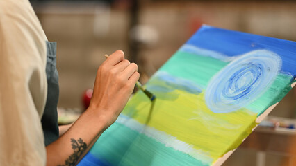 A close-up of a hand painting vibrant strokes on a canvas, blending blue, green, and yellow hues, showcasing creativity and the intricate details of artistic process