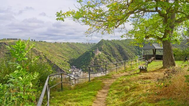 Following trail toward edge of majestic park viewpoint over the Rhine River Valley with a small town on the riverbanks and a castle, St. Goar, Germany