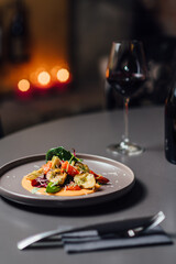 Delicious Roasted Vegetable Salad on Vibrant Orange Sauce Dish. Vertical composition with shallow depth of field, soft bokeh of candlelit background, paired with red wine