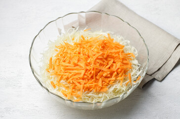 Freshly shredded white cabbage and grated carrot in glass bowl, for salad, fermentation, vegetable dishes, close up