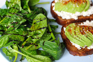 Rye toast with cottage cheese, avocado, sesame, flaxseeds, smoked paprika and pepper. Served with fresh spinach, lemon juice, olive oil, and balsamic vinegar on a blue plate. Healthy and delicious!