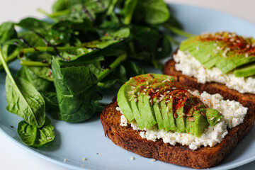 Rye toast with cottage cheese, avocado, sesame, flaxseeds, smoked paprika and pepper. Served with fresh spinach, lemon juice, olive oil, and balsamic vinegar on a blue plate. Healthy and delicious!