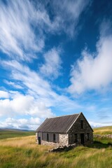 Obraz premium A historic stone cottage stands amidst lush green grass under a blue sky filled with fluffy white clouds in a serene landscape during the day