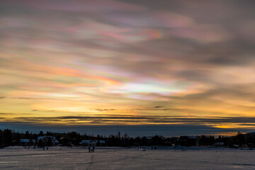 Beautiful winter sunset with rare nacreous clouds known as rainbow clouds over frozen lake...