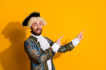 Smiling man in elegant historical attire pointing joyfully with both hands on an orange background