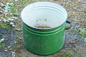 one large enameled kitchen capacious rusty with black handle shiny dirty green open empty old retro round saucepan stands on the ground during the day outdoors