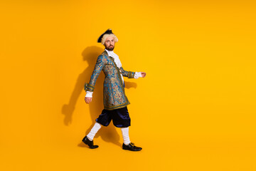 Portrait of a man in vintage royal attire walking against a vibrant yellow background