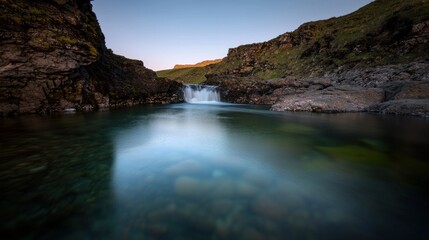 Serene waterfall cascading into a tranquil pool amidst rugged cliffs at sunset, capturing nature's beauty