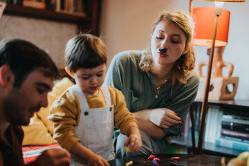 Family members are seen enjoying bonding time, engaging in playful activities in a comfortable and warm indoor setting, emphasizing affection, creativity, and togetherness.