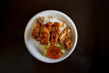 A plate of fried chicken with rice and a tomato on top. The plate is white and the food is brown