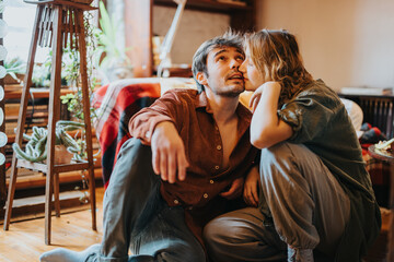 A couple sits closely in a snug and stylishly decorated living space, sharing a special bond. The...