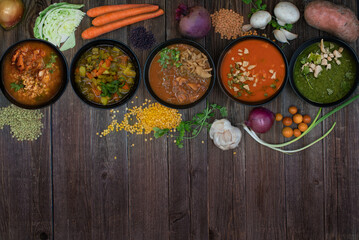An assortment of vegan soup bowls with scattered ingredients on wooden table, copy space